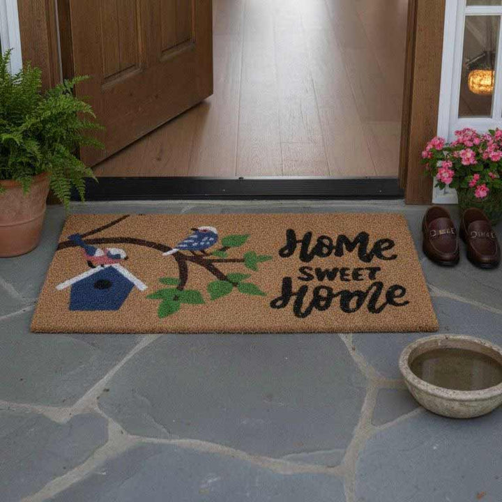Doormat with 'Home Sweet Home' text and bird design on a stone porch.