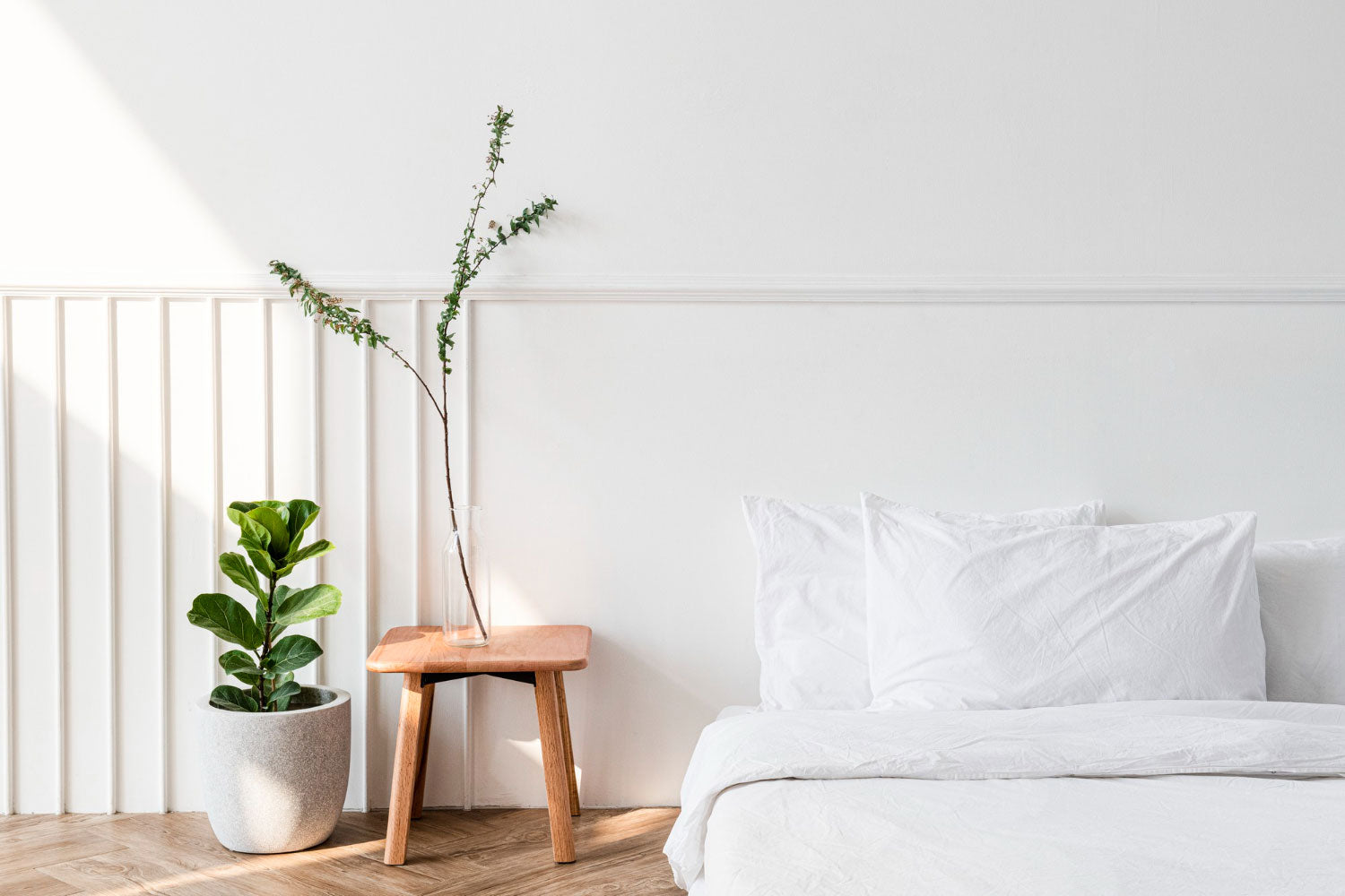 Minimalist bedroom with a bed, plant, and small wooden stool.