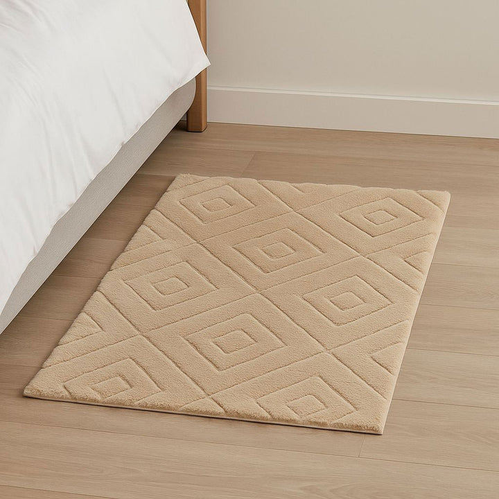 Beige diamond-patterned rug on a wooden floor next to a bed