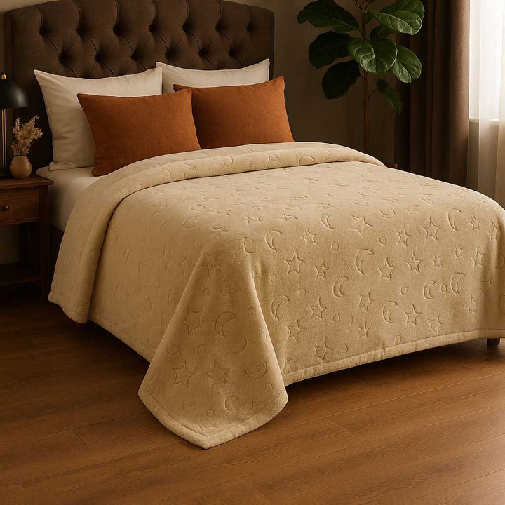 Beige blanket with star and moon patterns on a bed in a bedroom setting.