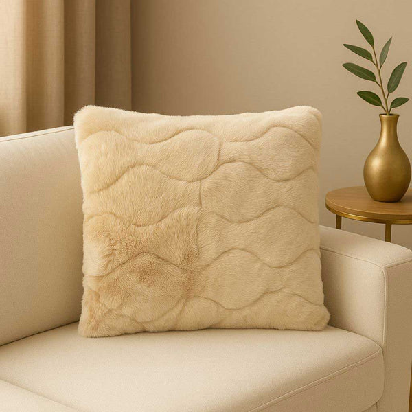 Beige textured pillow on a beige sofa with a gold vase and plant in the background.