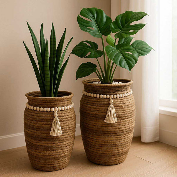 Two woven planters with tassels holding plants on a wooden floor.