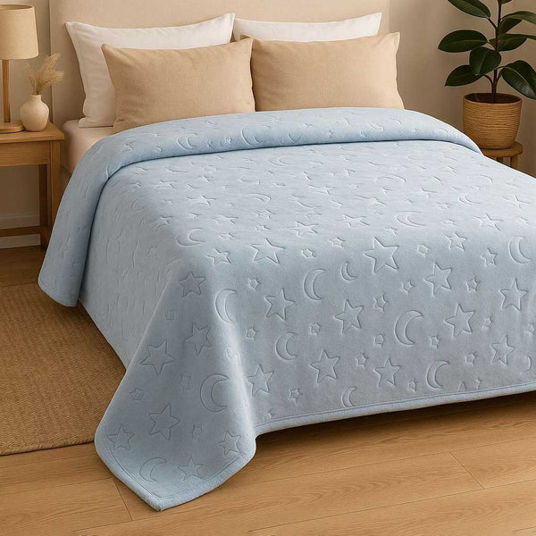 Light blue blanket with star and moon patterns on a bed in a bedroom setting.