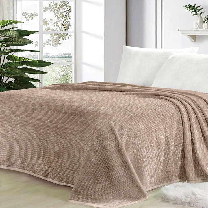 Beige quilt on a bed in a bright bedroom with plants and a window.
