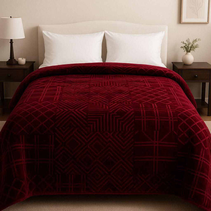Burgundy patterned winter blanket on a bed in a bedroom setting with nightstands and lamps.