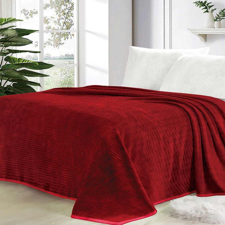 Red blanket draped over a bed in a bright room with plants and a window.