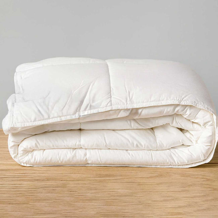 White quilt on a wooden bed frame with a gray background