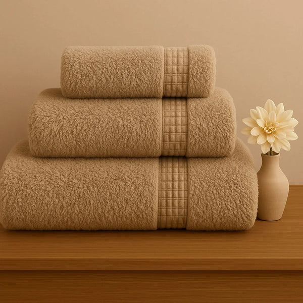 Stack of champagne beige towels on a wooden surface with a vase and flower in the background