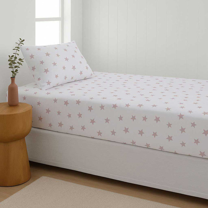Bed with star-patterned sheet set in a room with a wooden side table and plant.