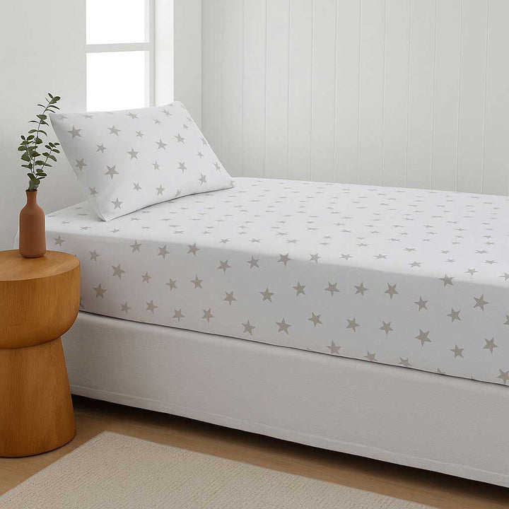 Bed with star-patterned sheet set in a room with a wooden side table and plant.