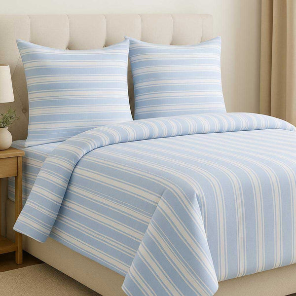 Blue and white striped bedding set on a bed with a beige headboard.