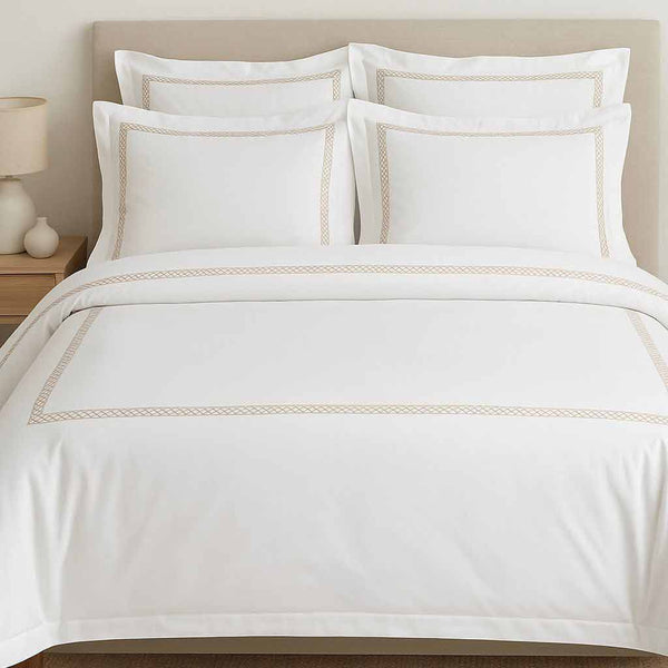 White bedding set with gold embroidery on a bed in a bedroom setting.