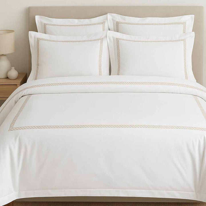 White bedding set with gold embroidery on a bed in a bedroom setting.