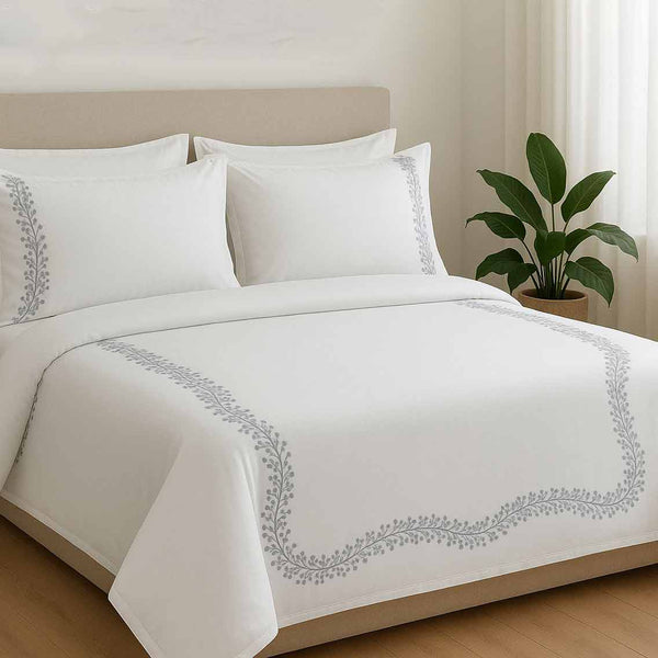 White duvet cover set with gray embroidery on a bed in a room with a plant.