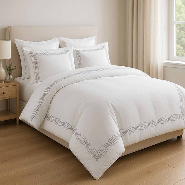 White bedding set with decorative patterns on a bed in a well-lit bedroom.