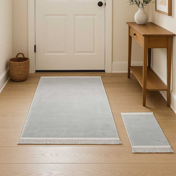 Two light gray area rugs on a wooden floor with a door and small table in the background.