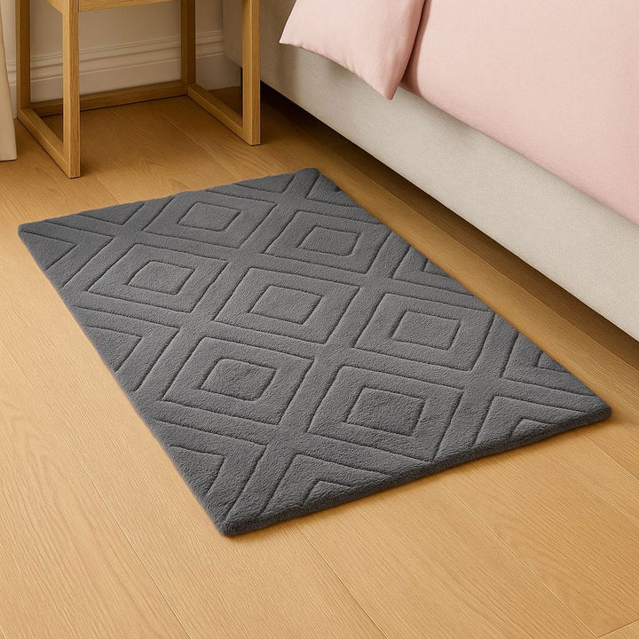 Gray geometric patterned rug on a wooden floor next to a bed with pink bedding.