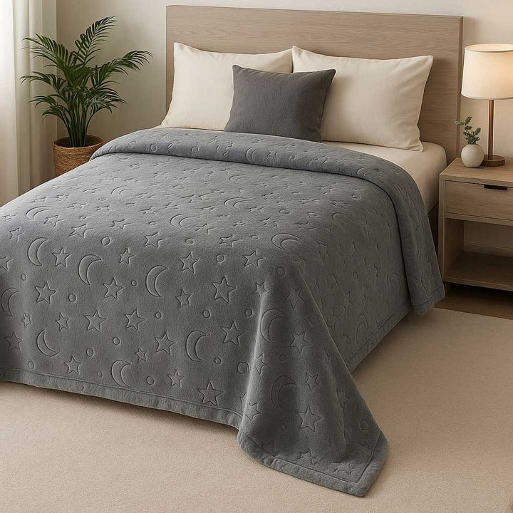 Gray textured blanket on a bed with star and moon patterns in a bedroom setting.