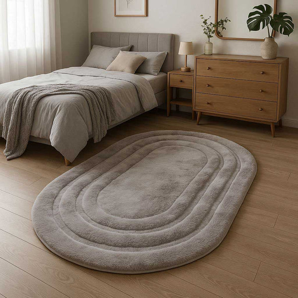 Gray oval rug on a wooden floor in a bedroom setting with a bed and dresser.