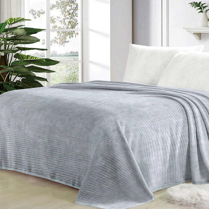 Gray blanket on a bed in a bright room with plants and a window.