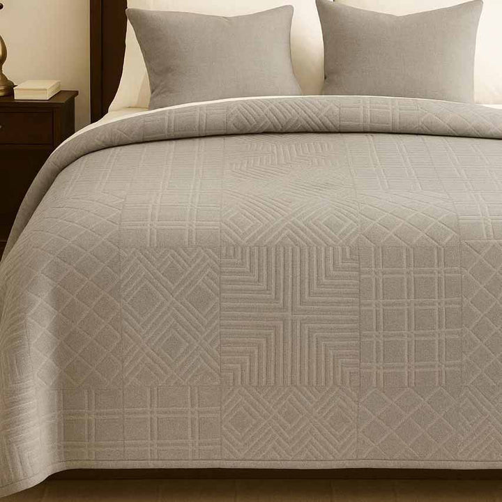 Greige metric patterned winter blanket on a bed with pillows and nightstand.