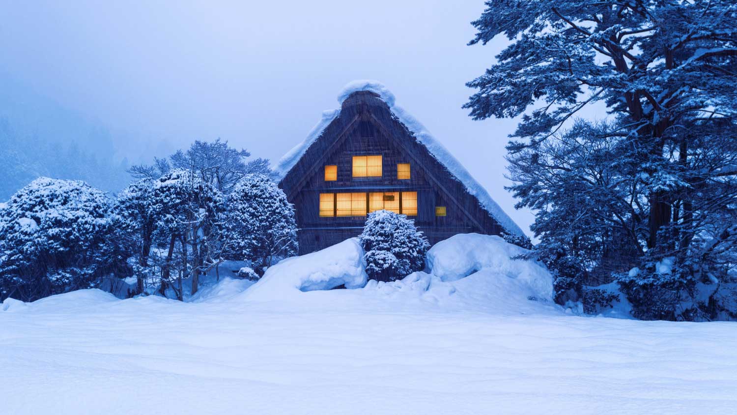 Snow-covered house with glowing windows in a winter landscape