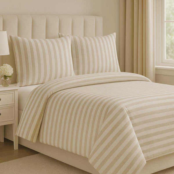 Beige striped bedding set on a bed in a bedroom with a nightstand and lamp.