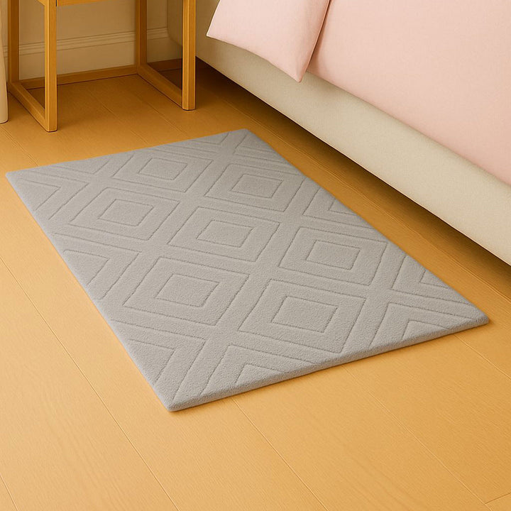 Gray geometric-patterned rug on a wooden floor with a bed in the background