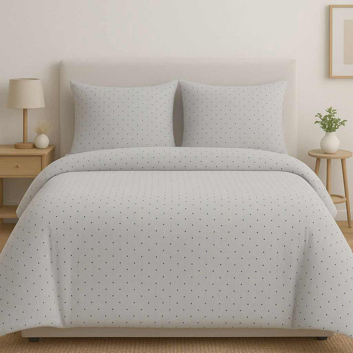 Gray polka dot comforter set on a bed in a bedroom setting with nightstands and a lamp.
