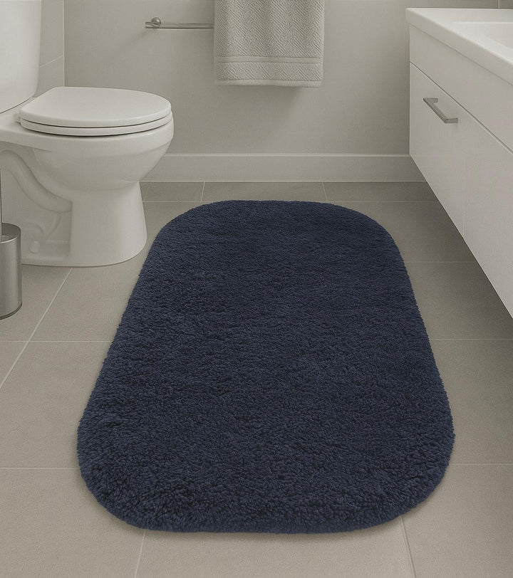 Navy blue bath mat on a bathroom floor with a toilet and sink in the background.