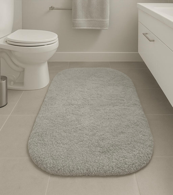 Gray bath mat on a bathroom floor with a toilet and sink in the background.