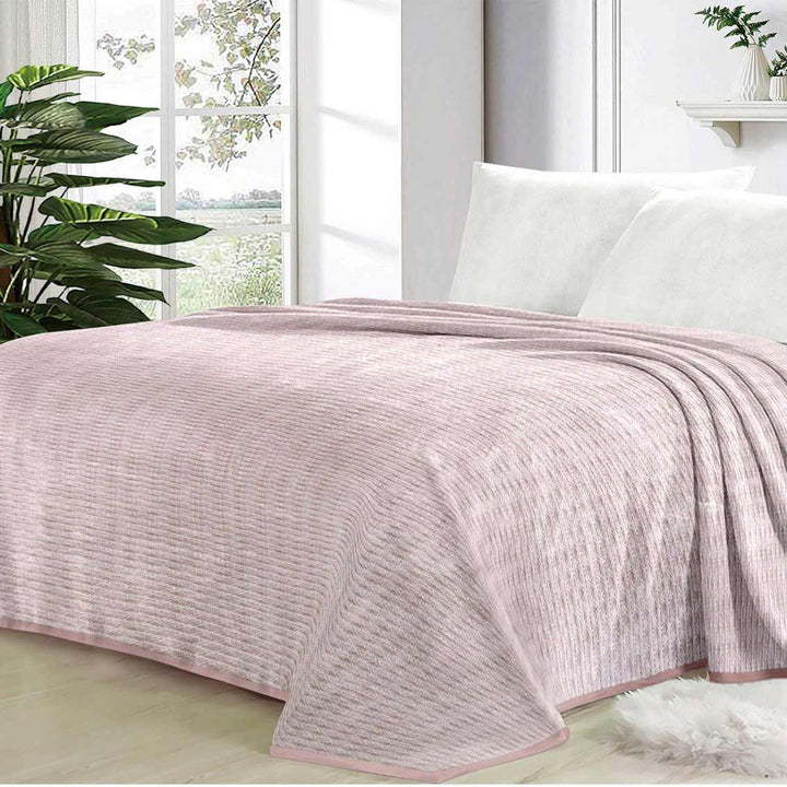 Pink textured blanket on a bed with a window and plants in the background