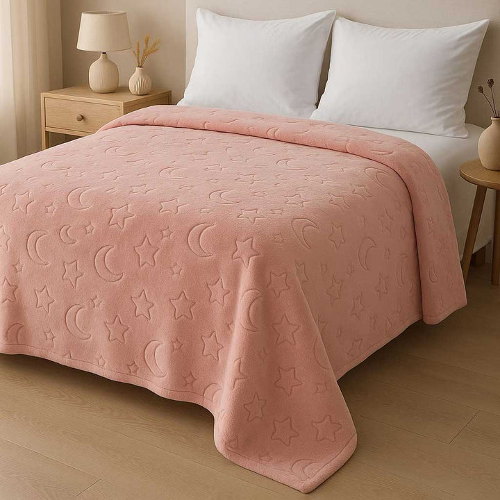 Pink blanket with star and moon patterns on a bed in a bedroom setting.