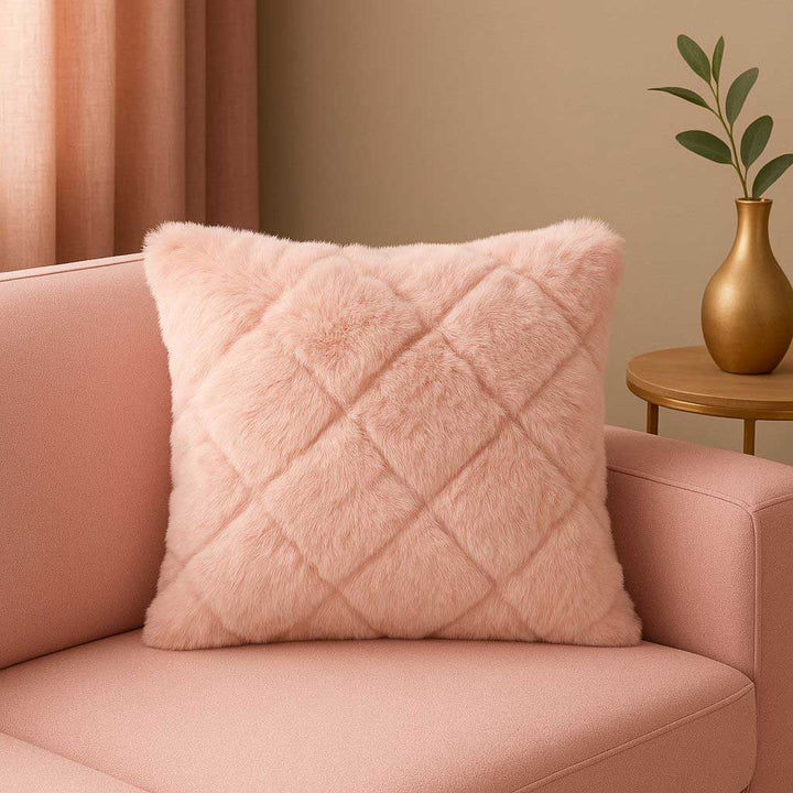 Pink fluffy pillow on a pink sofa with a gold vase and plant in the background.