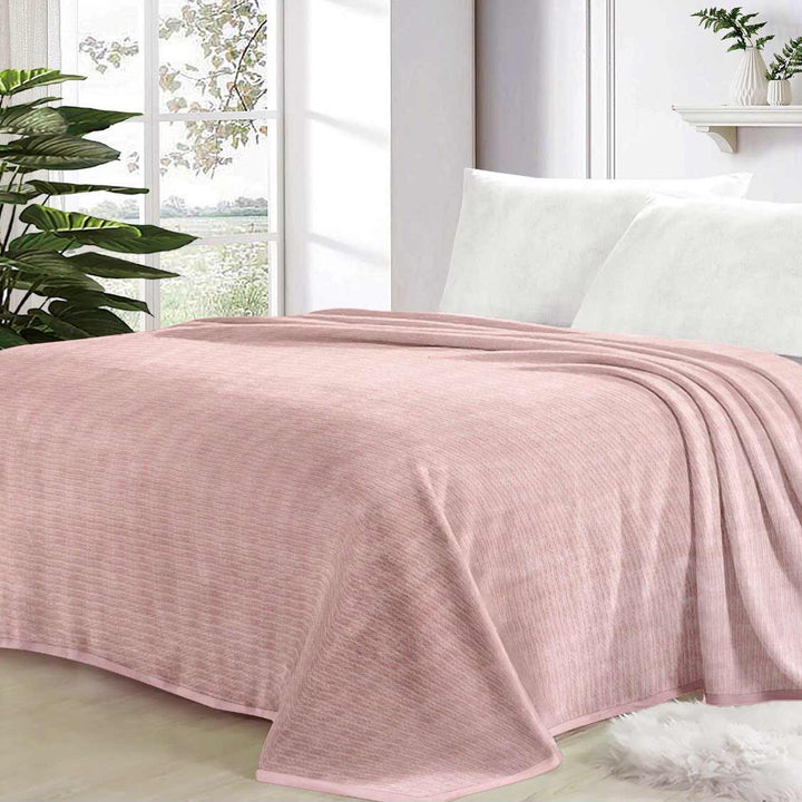 Pink blanket on a bed with white pillows and a window in the background