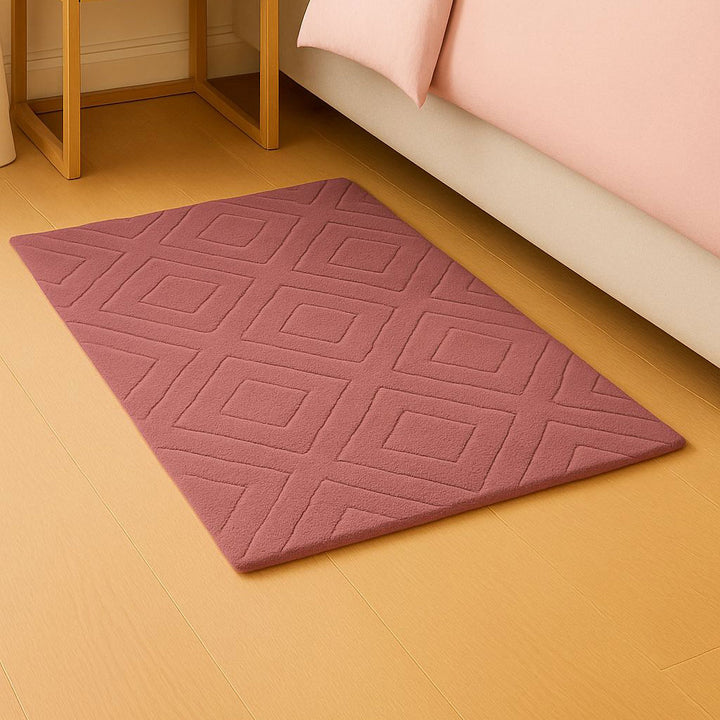 Pink textured rug on a wooden floor next to a bed with pink bedding.