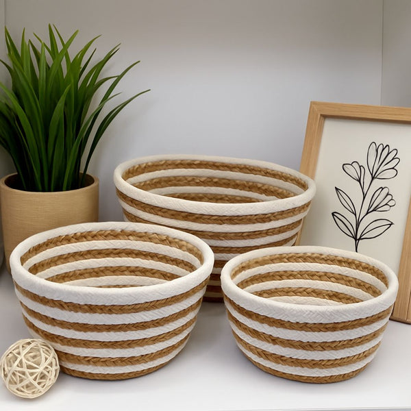 Three woven baskets with striped pattern on a white surface, with a plant and framed picture in the background.