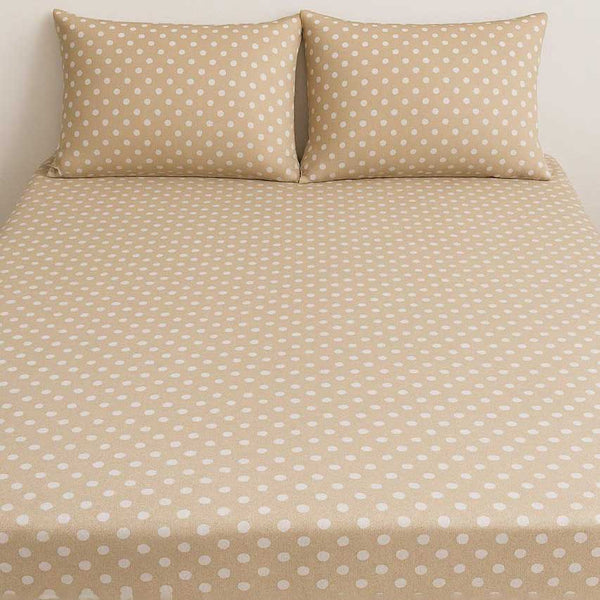Beige bed sheet with white polka dots and matching pillows on a plain background