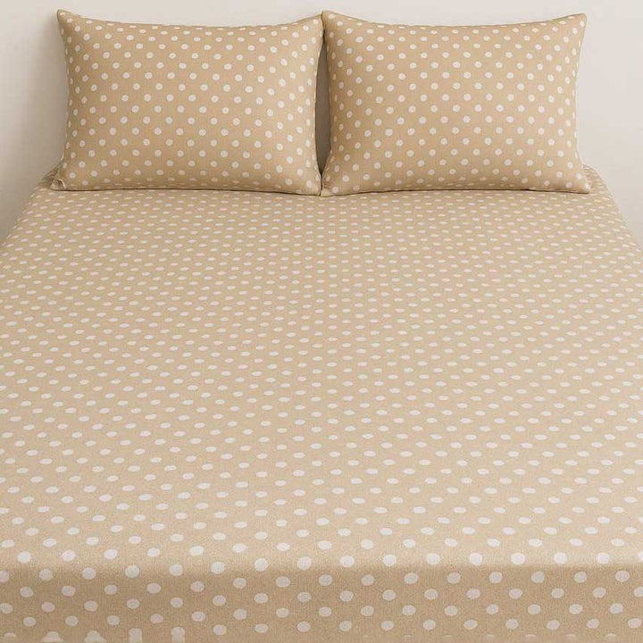 Beige bed sheet with white polka dots and matching pillows on a plain background