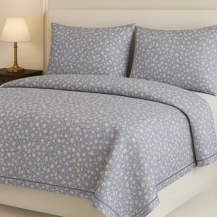 Blue floral patterned bedding set on a bed with a lamp in the background.