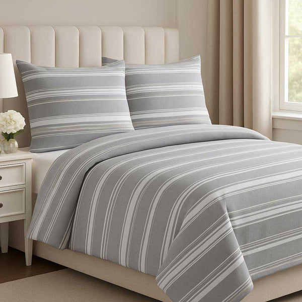 Gray striped bedding set on a bed in a bedroom with a lamp and window.