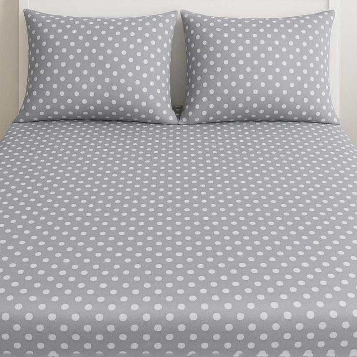 Gray bed sheet with white polka dots and matching pillowcases on a neutral background