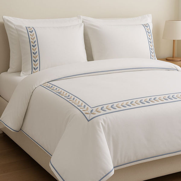 White bed set with embroidered border on a bed in a bedroom setting.