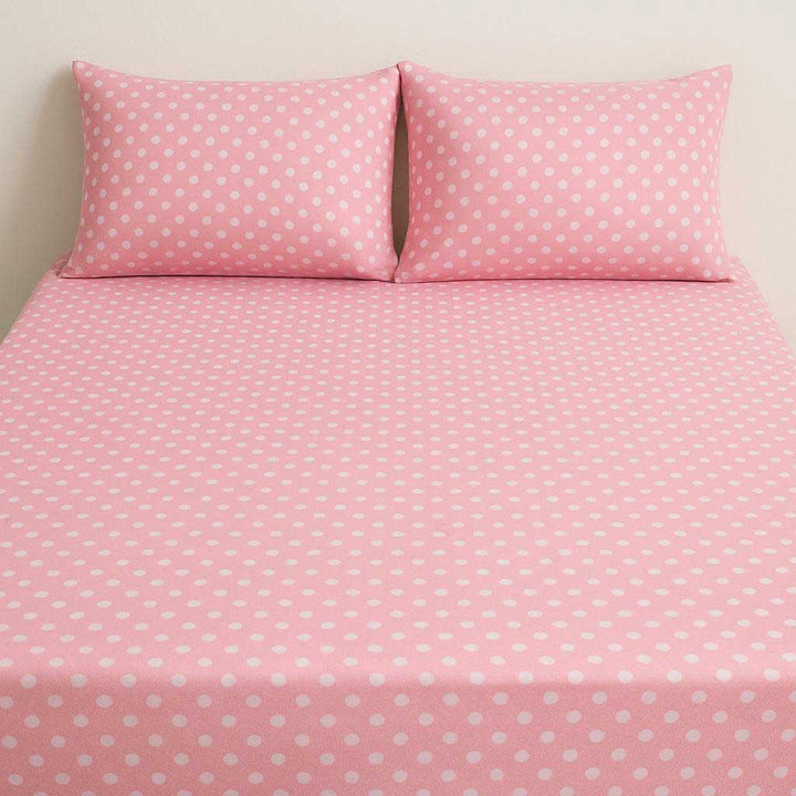 Pink polka dot bed sheet set with two pillows on a beige background