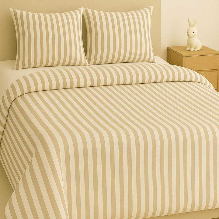 Beige and white striped bedding set on a bed with a wooden nightstand.