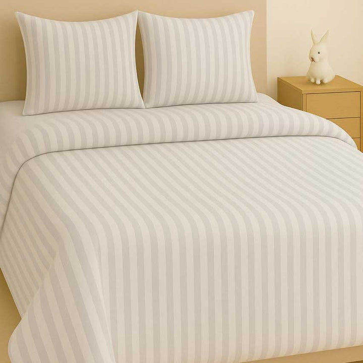 Striped bedding set on a bed with pillows and a nightstand in the background.