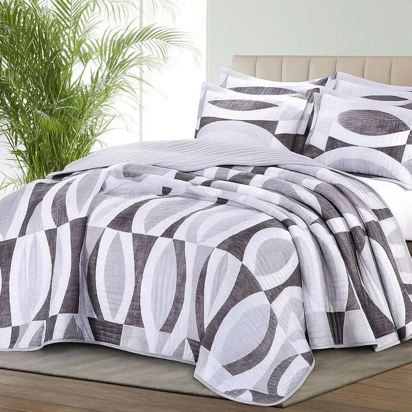 Bed with a geometric patterned bedspread set in a room with a plant.