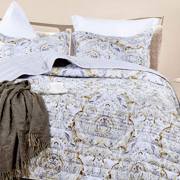 Elegant summer bedspread with a grey and gold damask medallion pattern, styled on a bed with matching shams, a fringed throw, and a white teacup
