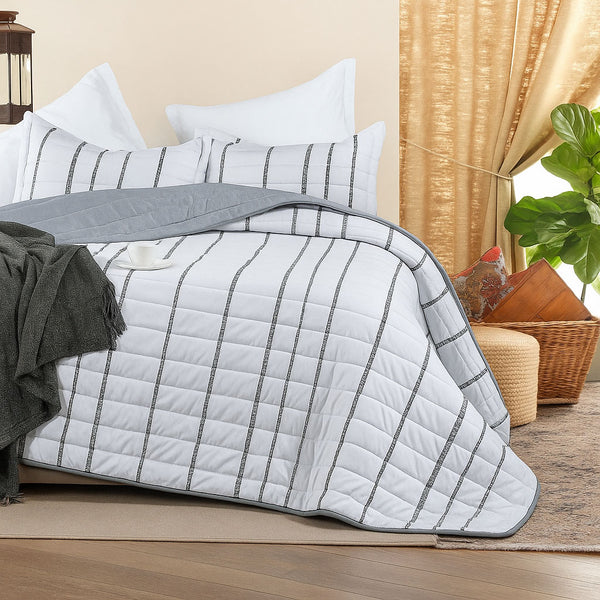White summer bedspread with vertical black stitched stripes, styled with matching pillows, a grey throw, and gold curtains in a cozy bedroom