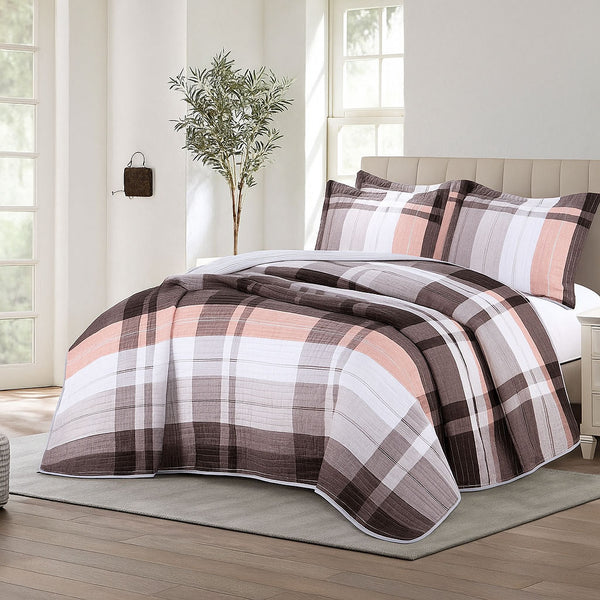 Plaid summer bedspread in brown, white, and soft pink tones, styled with matching pillow shams in a bright room with tall windows and minimal decor